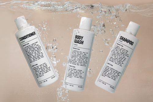 Three white bottles labeled Conditioner, Body Wash, and Shampoo float in water, each showcasing detailed black text against a beige background. Infused with Argan Oil and enriched with Natural Ingredients by Blu Atlas for a nourishing experience. Product Name: Shower Refresh Set - Nift.