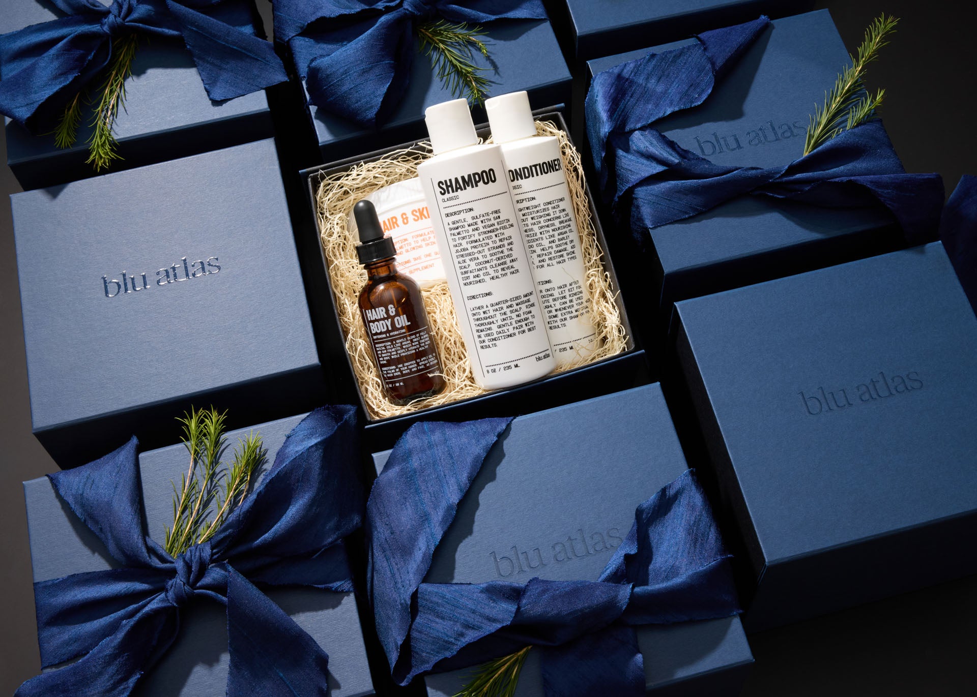 The Ultimate Hair Care Set by Blu Atlas features clean ingredients and includes shampoo, conditioner, and hair & body oil elegantly packaged in blue boxes adorned with matching blue ribbons—perfect for nurturing both hair and scalp.