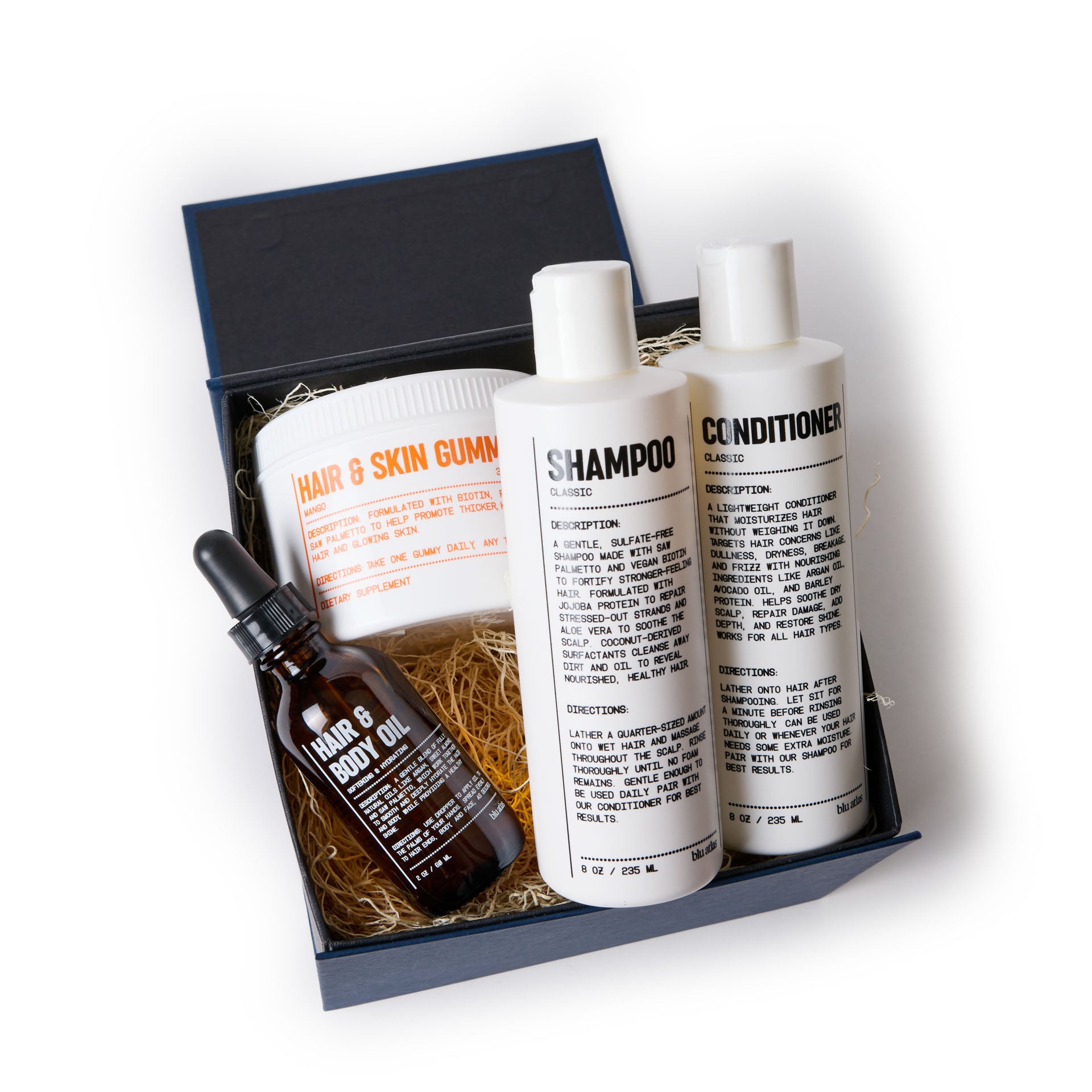 The Ultimate Hair Care Set by Blu Atlas presents a luxurious collection featuring shampoo, conditioner, hair & body oil, and a jar of hair & skin gummies made with clean ingredients, all beautifully arranged on a bed of straw-like material.
