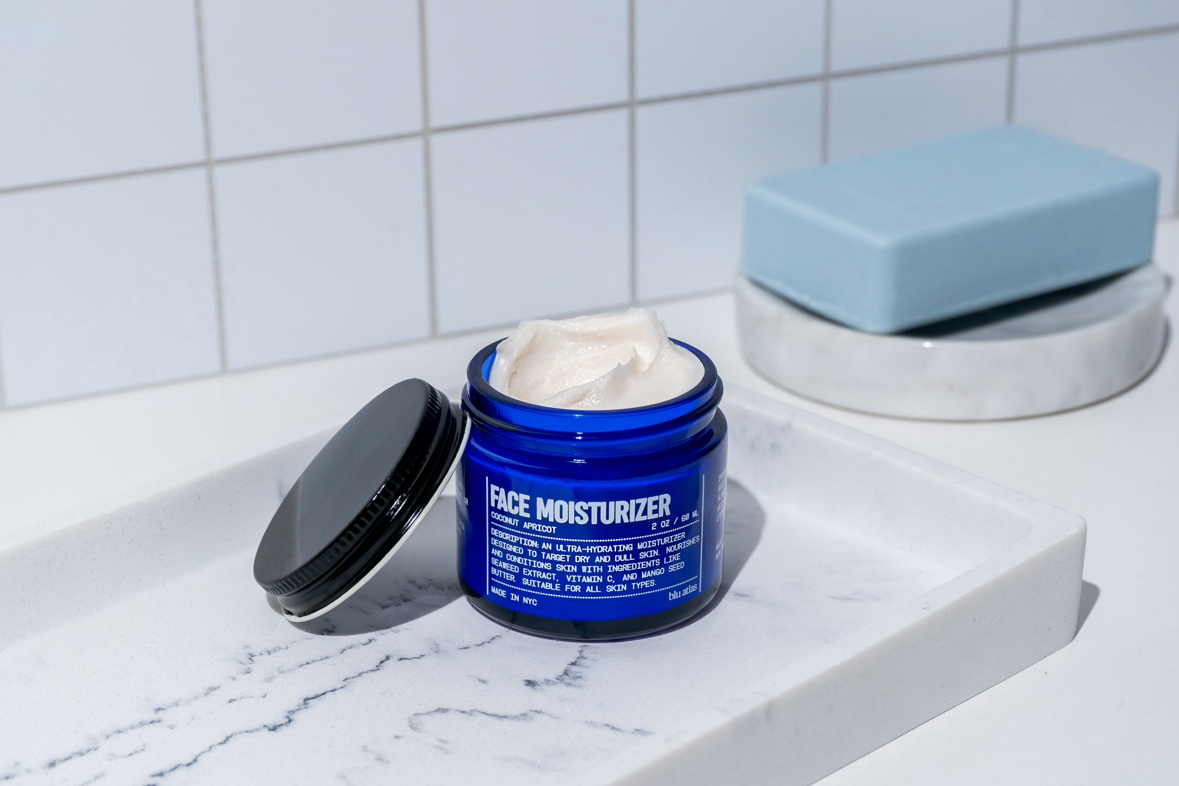 Blue jar of face moisturizer on a marble surface with a white tiled wall background