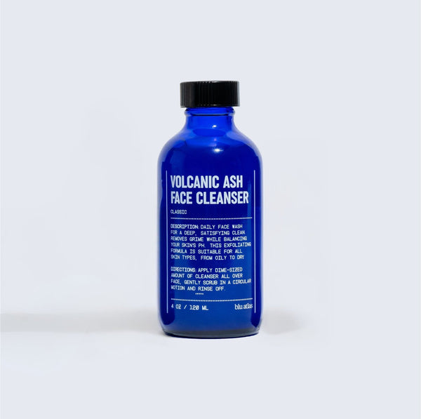 A blue bottle of Blu Atlas Volcanic Ash Face Cleanser, a fragrance-free exfoliating face wash, stands upright against a plain light background.