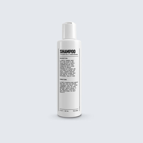A bottle of Blu Atlas Natural Shampoo for All Hair Types features black text detailing its description, instructions, and ingredients on a white background and is enriched with vegan biotin for a nourishing cleanse.