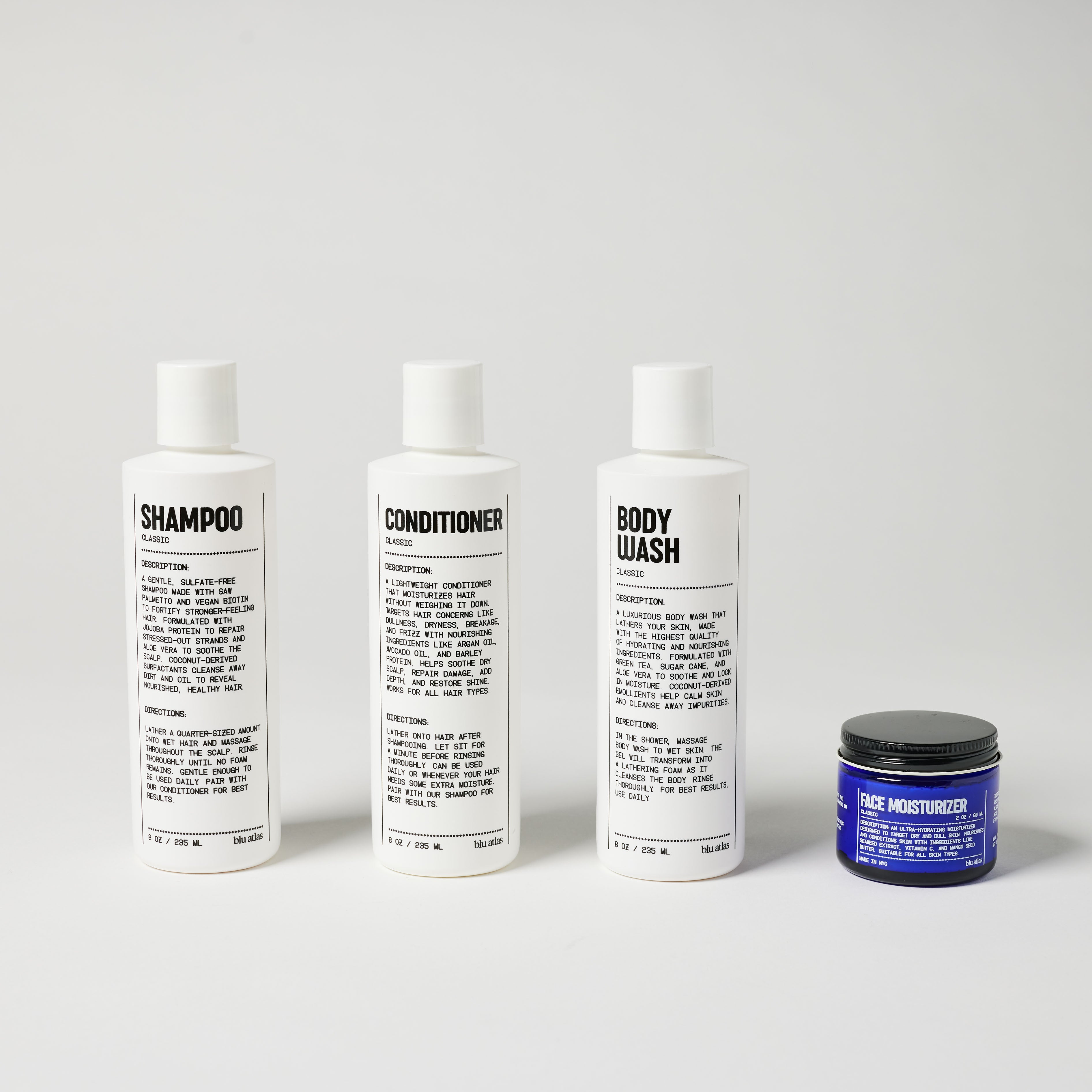 The Essentials Bundle by Blu Atlas features four personal care products: a scalp-soothing shampoo, a frizz-fighting conditioner, and an acne-preventing body wash, all in sleek white bottles. These are perfectly complemented by a face moisturizer presented in a sophisticated blue jar, all arranged neatly against a simple backdrop.