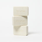 Three stacked bars of Blu Atlas Natural Exfoliating Bar Soap, enriched with jojoba beads, sit against a white background.