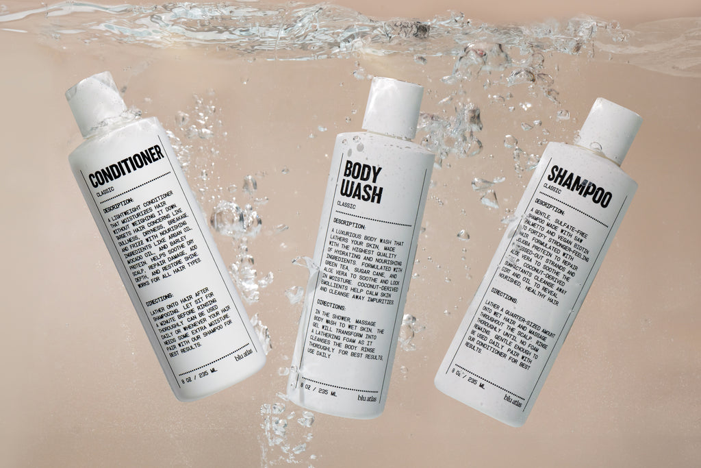 Three white bottles labeled conditioner, body wash, and shampoo float underwater with bubbles, showcasing the Blu Atlas Shower Refresh Set—a men’s grooming collection made with natural ingredients.