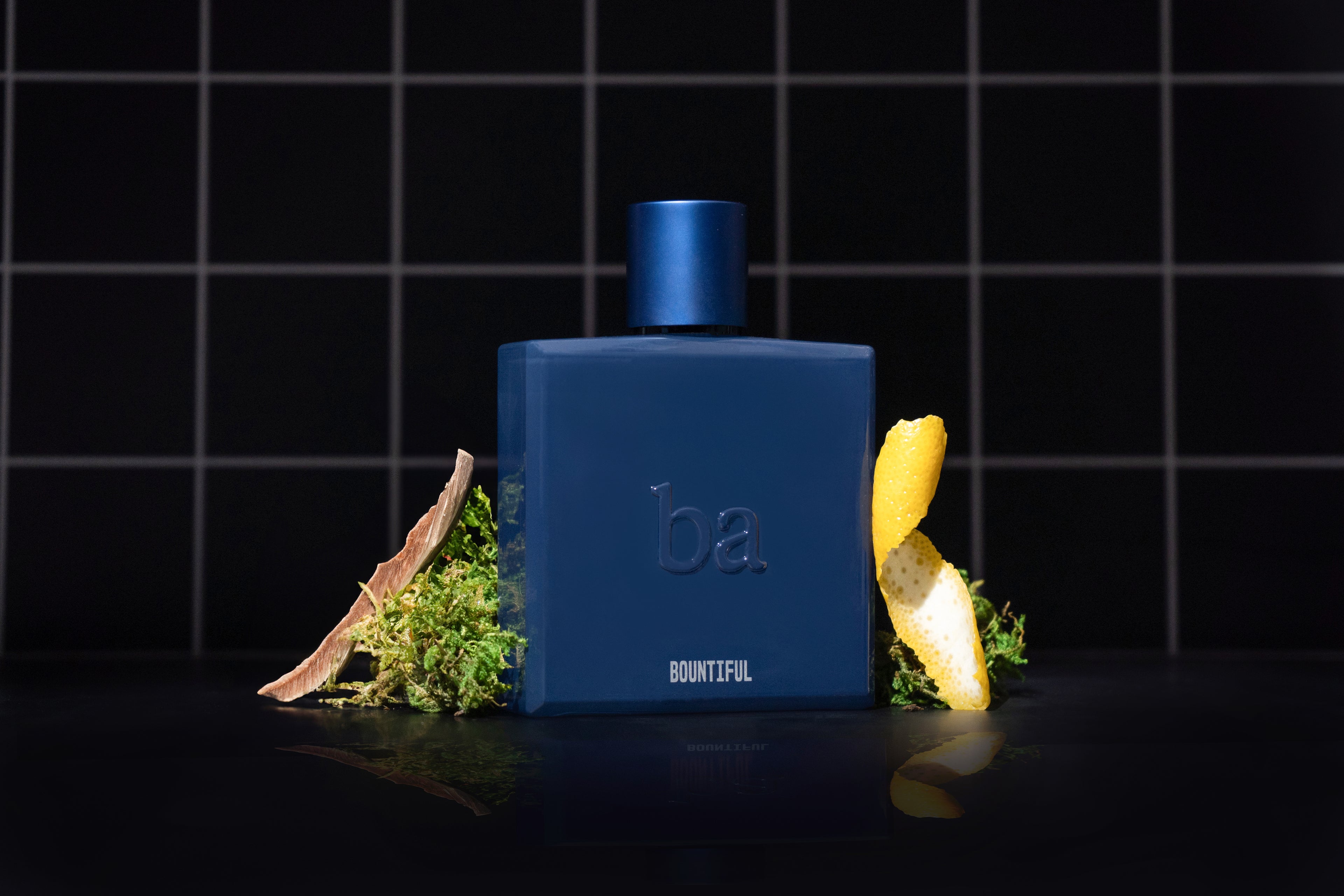 A bottle of Bountiful Eau de Parfum by Blu Atlas, with its enchanting fragrance of lemon peel and greenery, stands elegantly against a black tiled background.