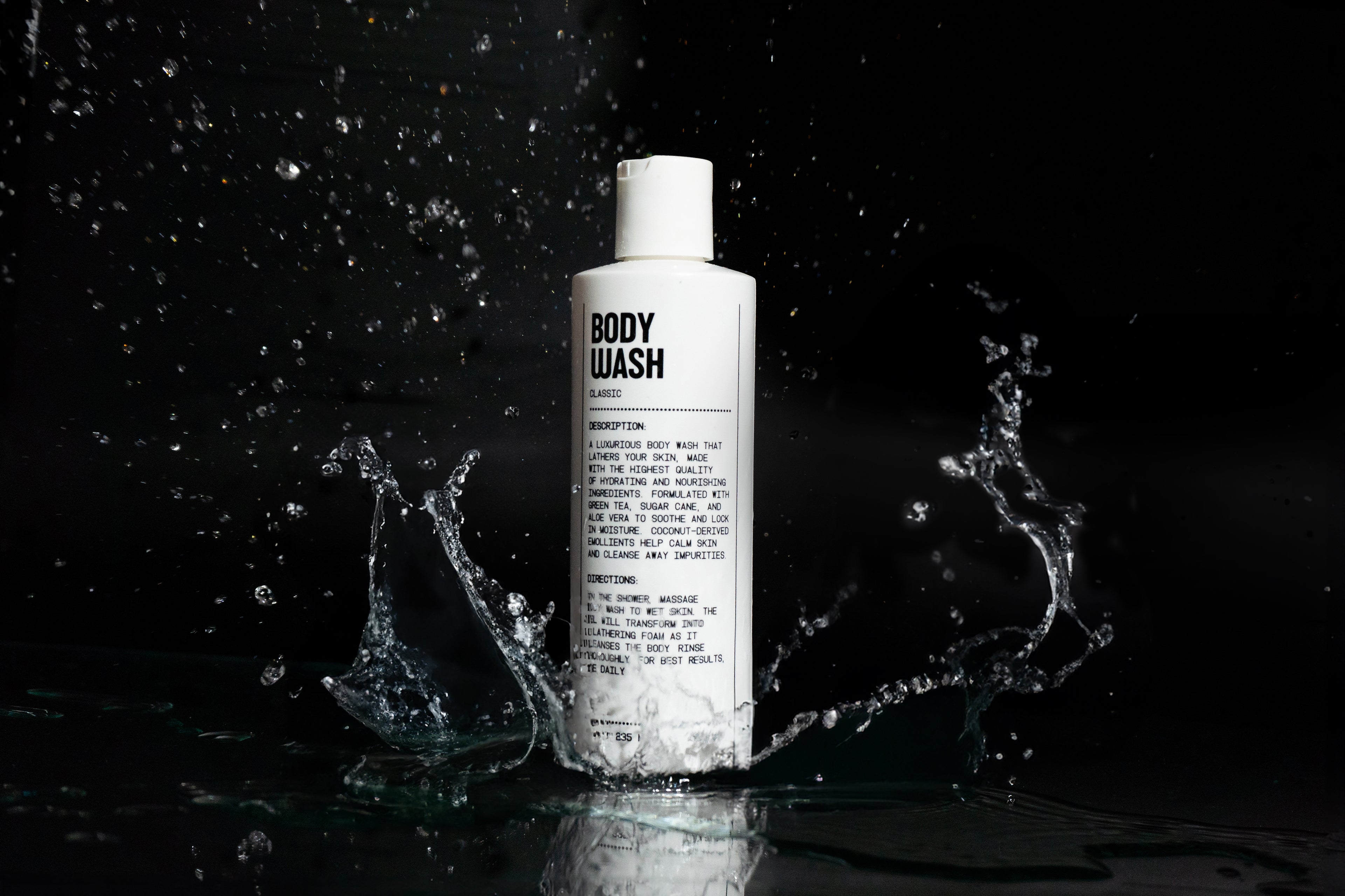 A white bottle labeled Blu Atlas Body Essentials stands upright on a reflective black surface with water splashing around it, emphasizing its skin hydration benefits.