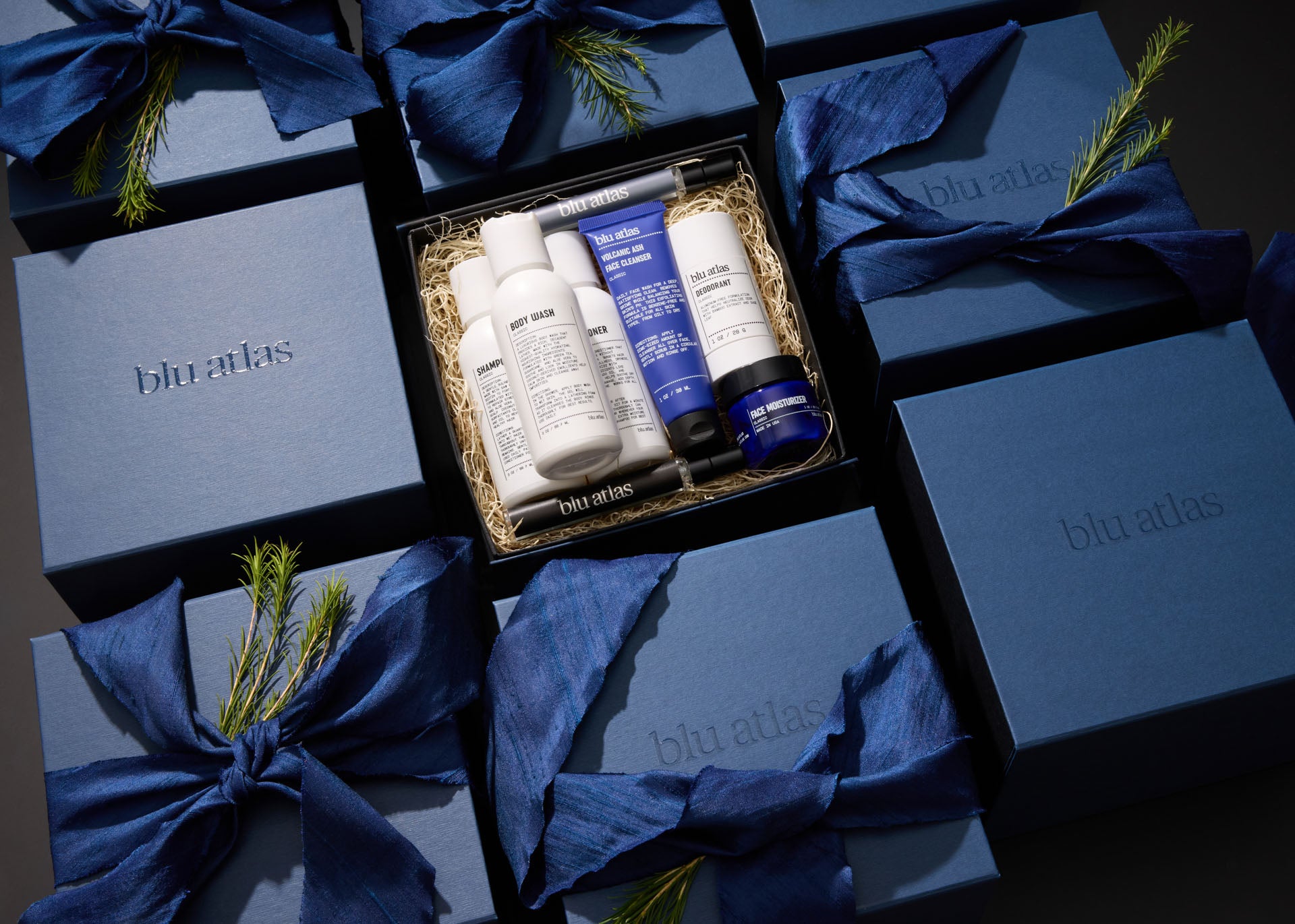 Explore the exclusive Mini MVP Grooming Essentials Bundle by Blu Atlas, a carefully curated selection of skincare products. Elegantly presented in a gift box and accompanied by other blue boxes adorned with ribbons and small pine branches, this bundle adds a perfect touch of luxury for any occasion.