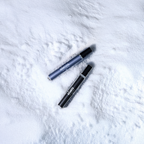 Two cylindrical cosmetic tubes from the Blu Atlas Fragrance Discovery Set, one blue and one black, rest on white snow.