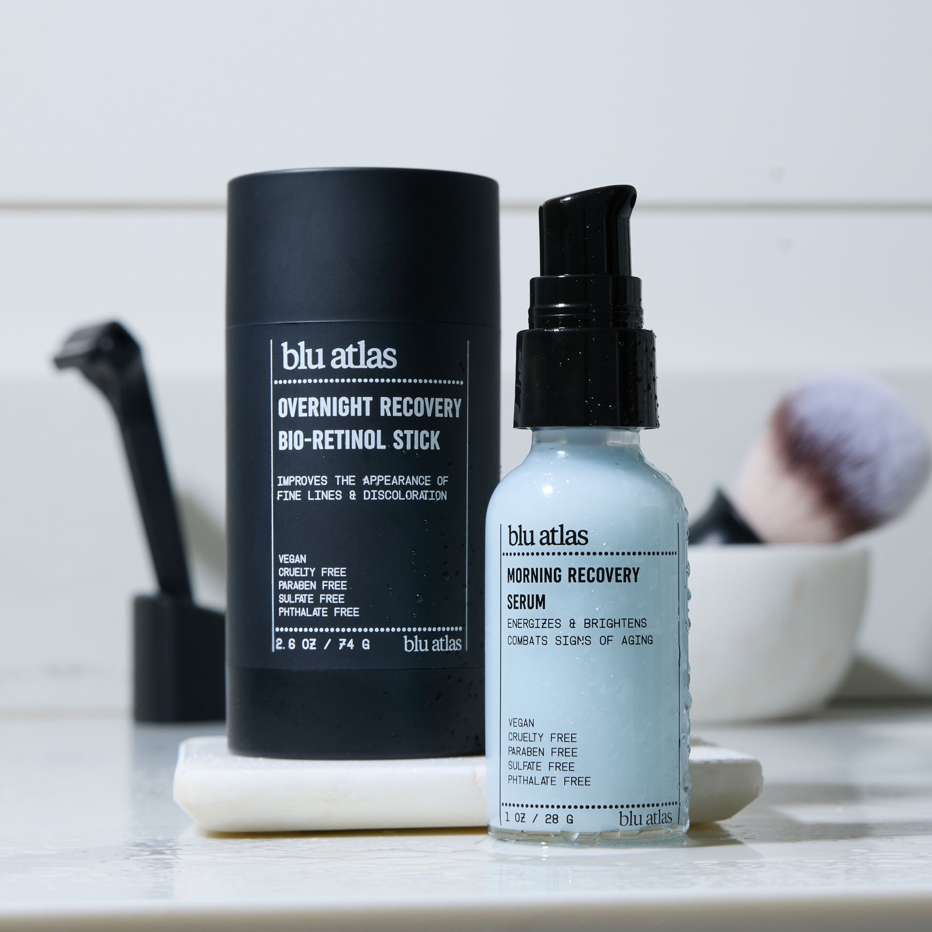 Blu Atlas Morning/Night Bundle features the Overnight Recovery Bio-Retinol Stick and Morning Recovery Serum for hydrated, firmer skin, shown on a white tray with a makeup brush and marble container in the background.
