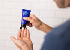 A person dispenses a small amount of Blu Atlas Protect & Moisturize Duo cream with UVA and UVB protection from a blue tube into their palm, set against a white tiled background.