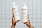 Two hands hold up white Blu Atlas pump bottles labeled Natural Shampoo - Coconut Apricot, with description text, against a tiled background.