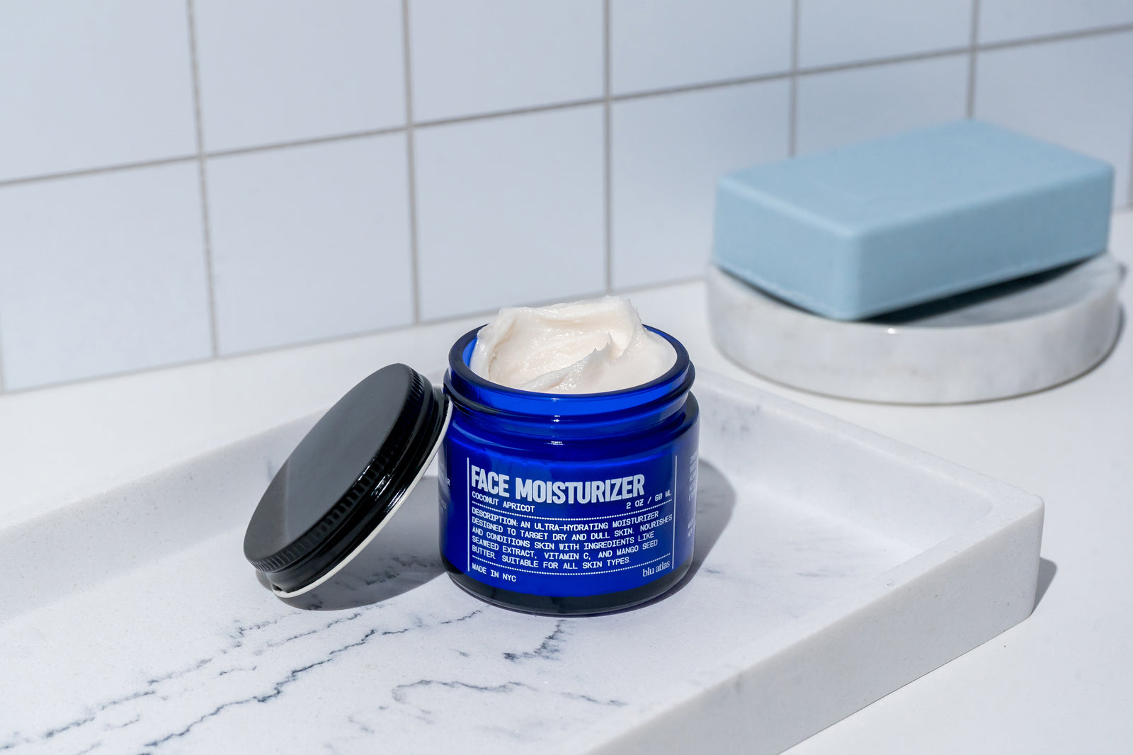 Blue jar of face moisturizer on a marble surface with a white tiled wall background