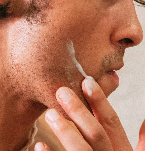 Close-up of a person applying cream to their face with a neutral background