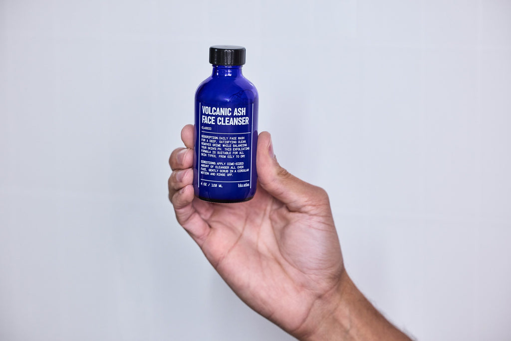 A hand holds the Blu Atlas Face Essentials (Cleanser + Moisturizer) set against a plain light background—your daily skincare must-have.