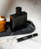 A sleek black perfume bottle, a small vial labeled "Travel Size Atlantis Eau de Parfum" by Blu Atlas, and a lit candle are artfully arranged on a black tray, evoking the allure of an aquatic fragrance with citrusy undertones.