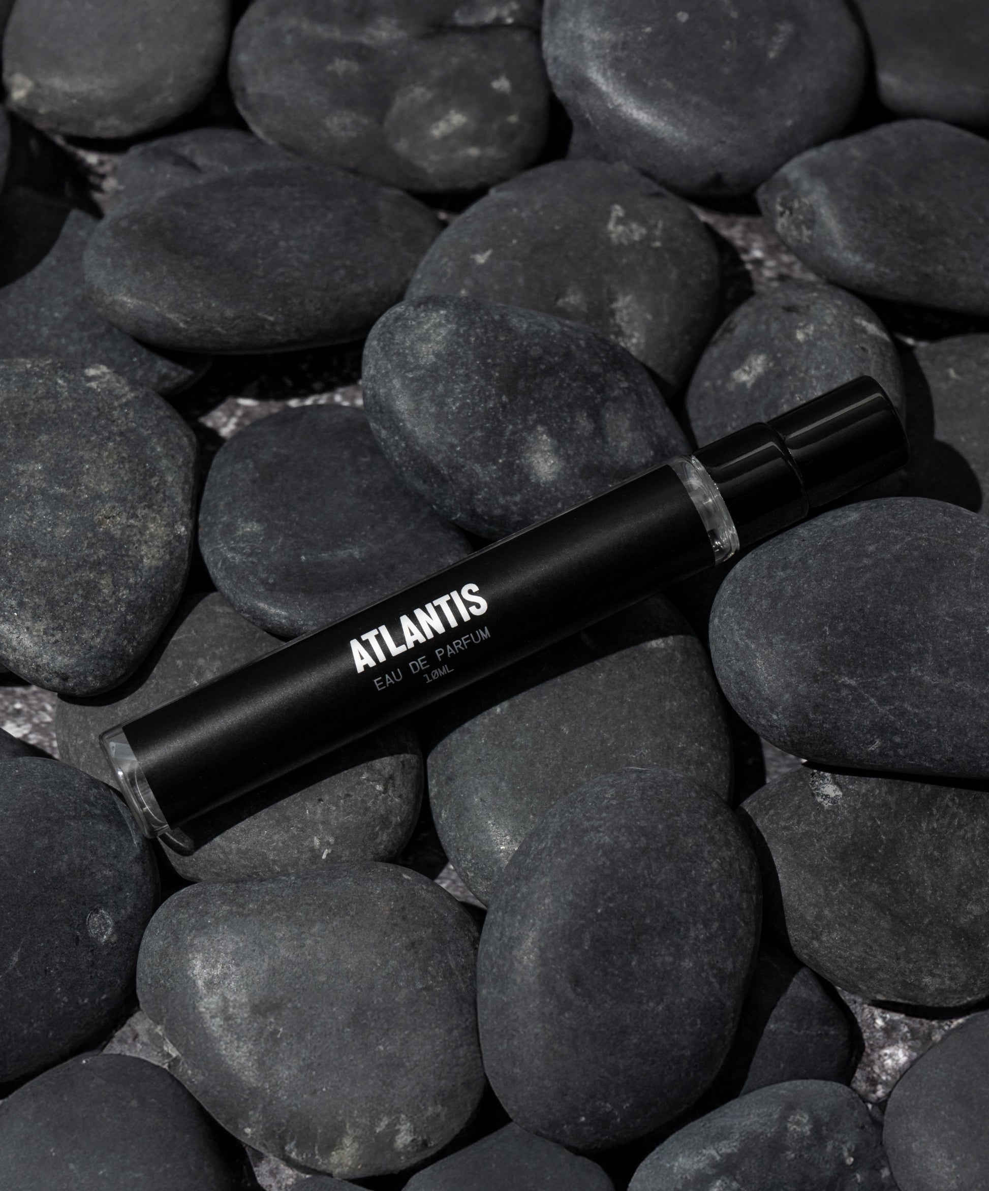 A black bottle labeled Travel Size Atlantis Eau de Parfum by Blu Atlas, with its aquatic fragrance, rests on smooth dark stones.