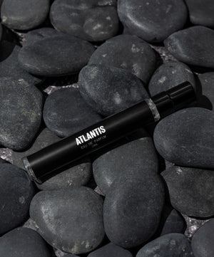 A black bottle labeled Travel Size Atlantis Eau de Parfum by Blu Atlas, with its aquatic fragrance, rests on smooth dark stones.