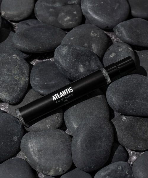 A black bottle labeled Travel Size Atlantis Eau de Parfum by Blu Atlas, with its aquatic fragrance, rests on smooth dark stones.