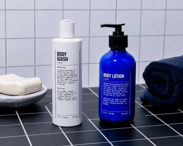 Blu Atlas Body Essentials (Wash & Lotion) sit beside a bar of soap and a dark blue towel on a tiled surface, perfect for your daily body care routine.