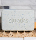 The Natural Exfoliating Bar Soap by Blu Atlas, featuring jojoba beads, rests on a stone soap holder in a stylish bathroom setting.