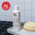 A bottle of Blu Atlas Hydrating Body Wash and a brush gracefully rest on a gray tray against the tiled wall, with an RS Recommends badge in the corner.