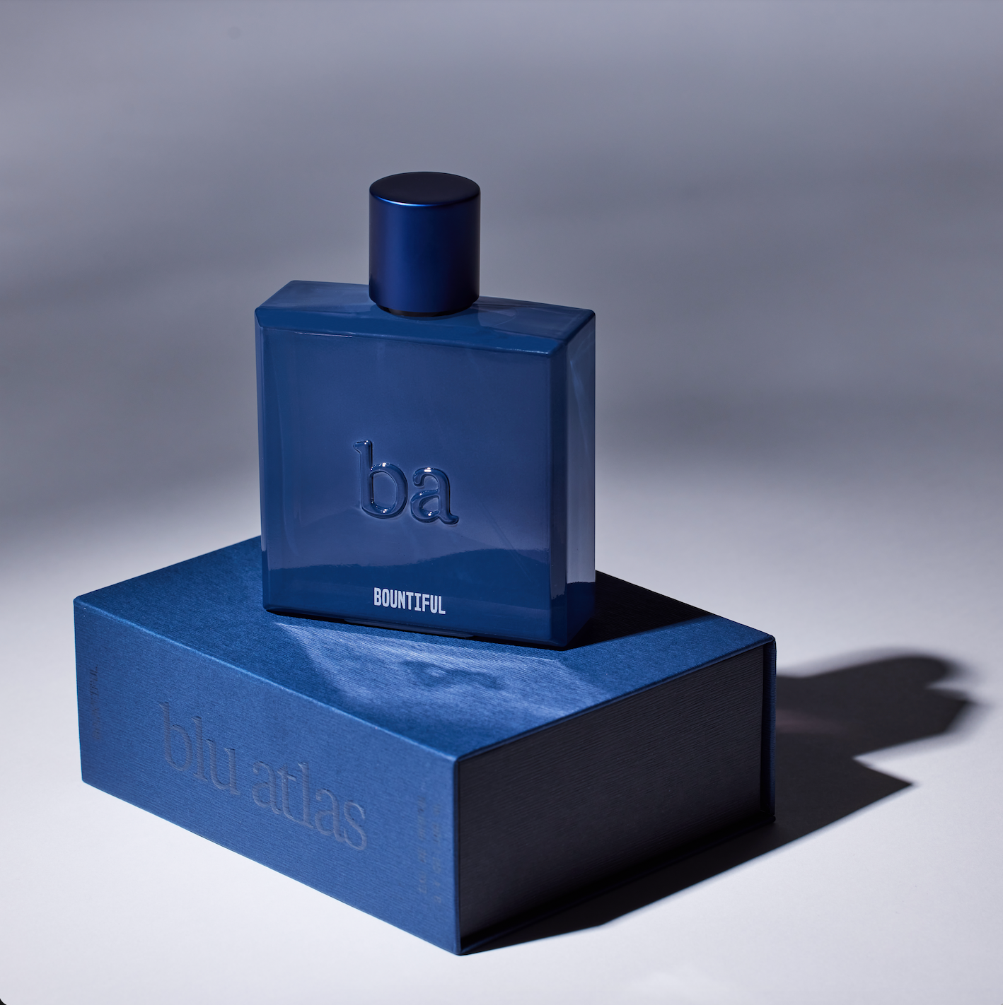 A blue perfume bottle titled Bountiful Eau de Parfum rests on a complementary Blu Atlas box against a gradient background, emanating an enchanting fragrance.