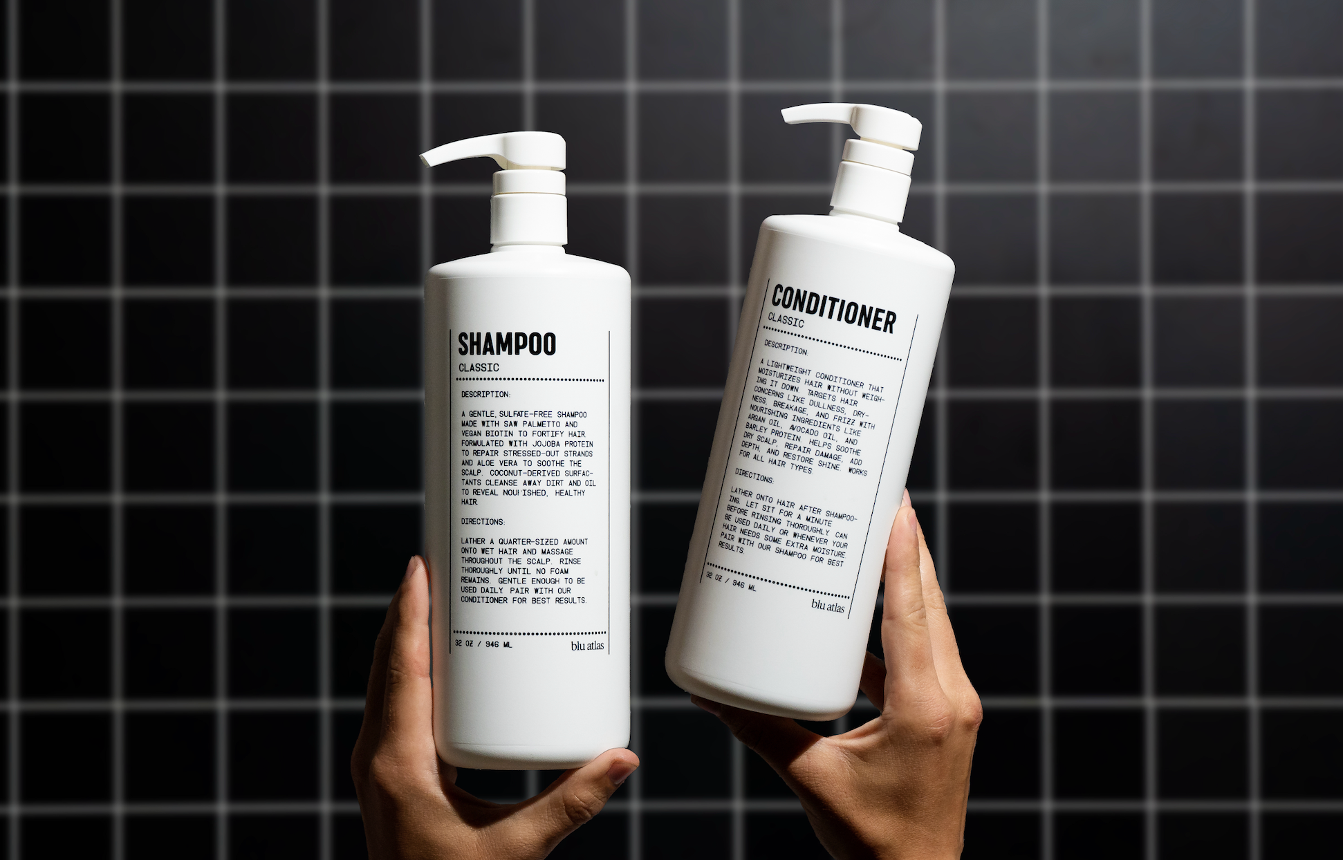 Two hands holding white bottles labeled Shampoo and Conditioner with pumps against a dark tiled background.