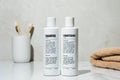 Two white Blu Atlas Hair Essentials bottles (Shampoo + Conditioner) rest on the bathroom counter, ideal for daily hair care. A cup of toothbrushes and a folded towel complete this clean vegan routine.