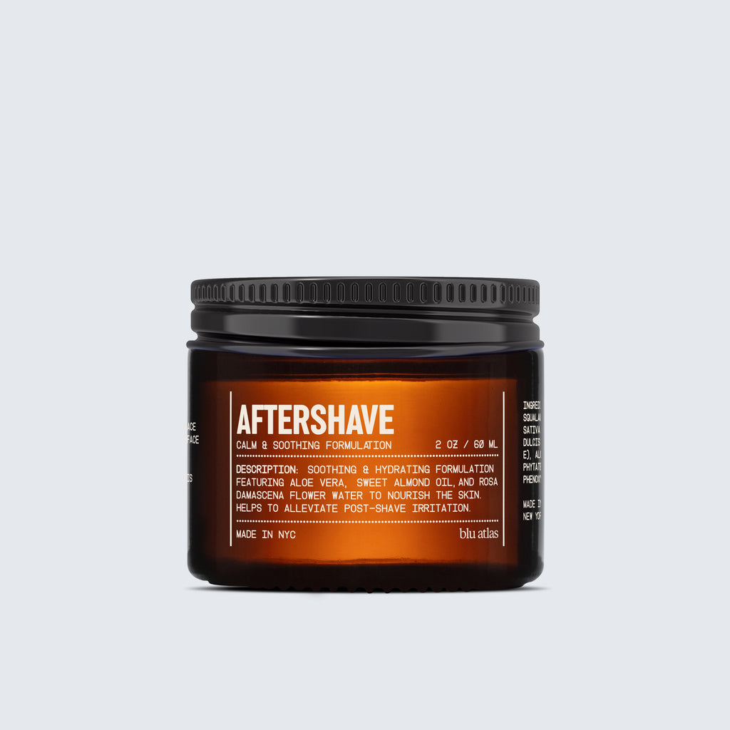 A brown jar labeled Blu Atlas Shave Essentials (Shave Cream + Aftershave) with white text features soothing aloe vera, hydrating almond oil, and a stearic-acid cushion for comfort, set against a plain light gray background.