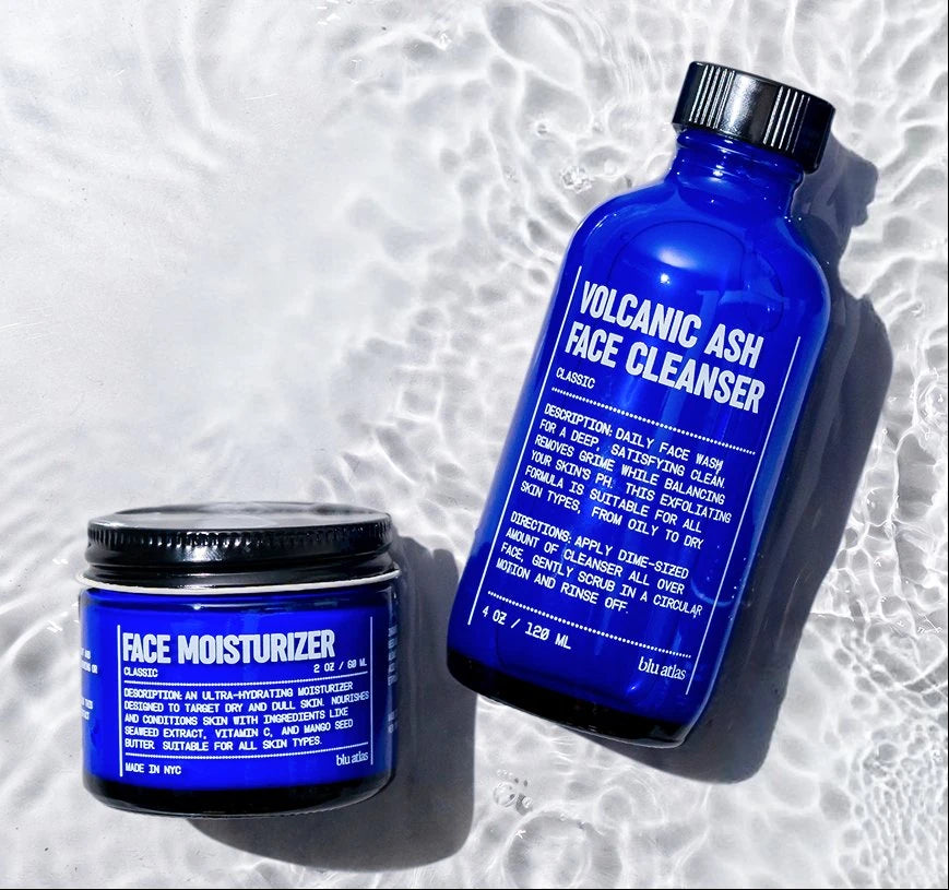 Blue facial cleanser bottle and moisturizer jar on a textured white background