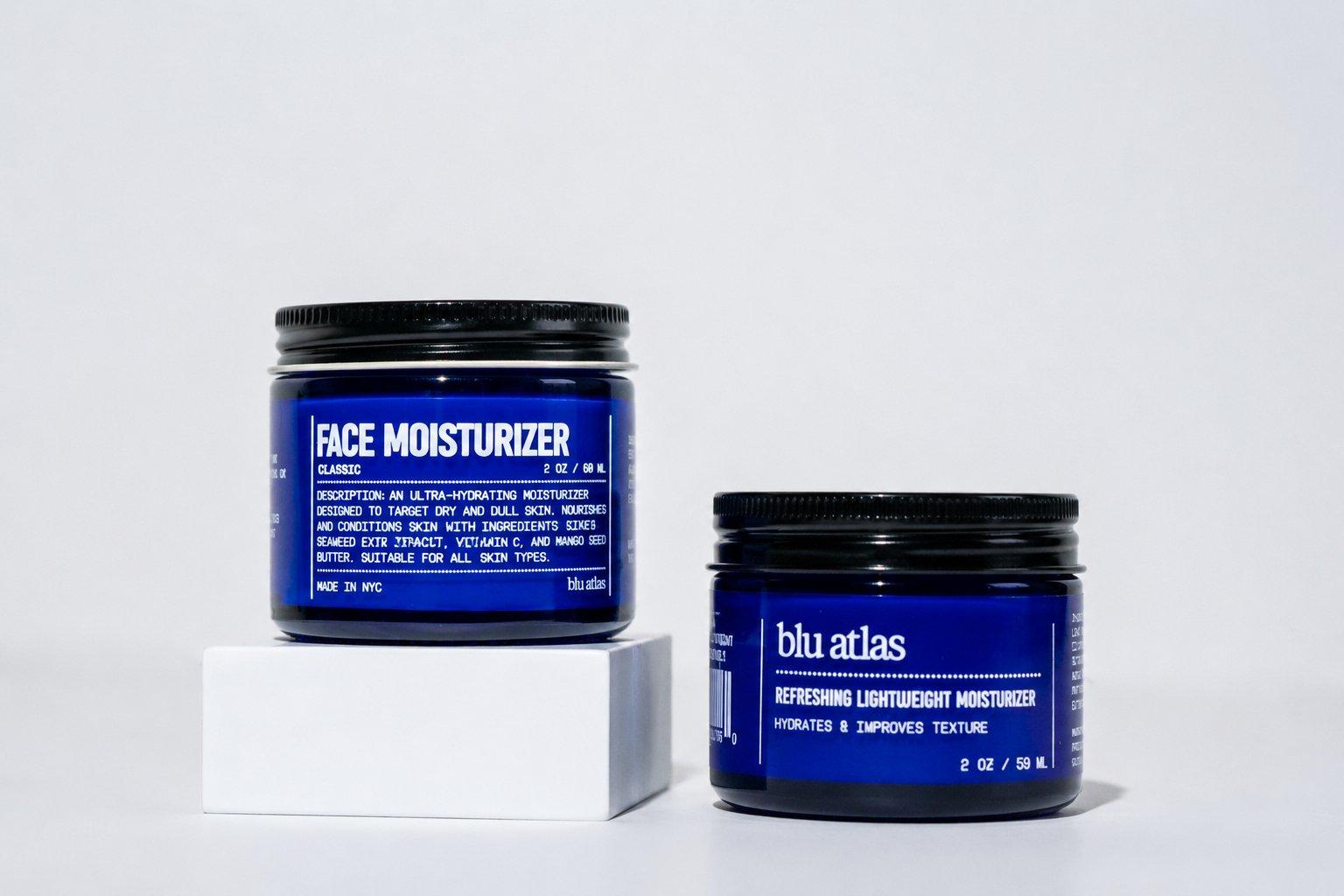 Two blue jars of moisturizer sit on a white background, with one jar elevated on a small white block. Both are Blu Atlas Natural Lightweight Face Moisturizer gel moisturizers—perfect for oily skin, providing lightweight hydration without feeling heavy.