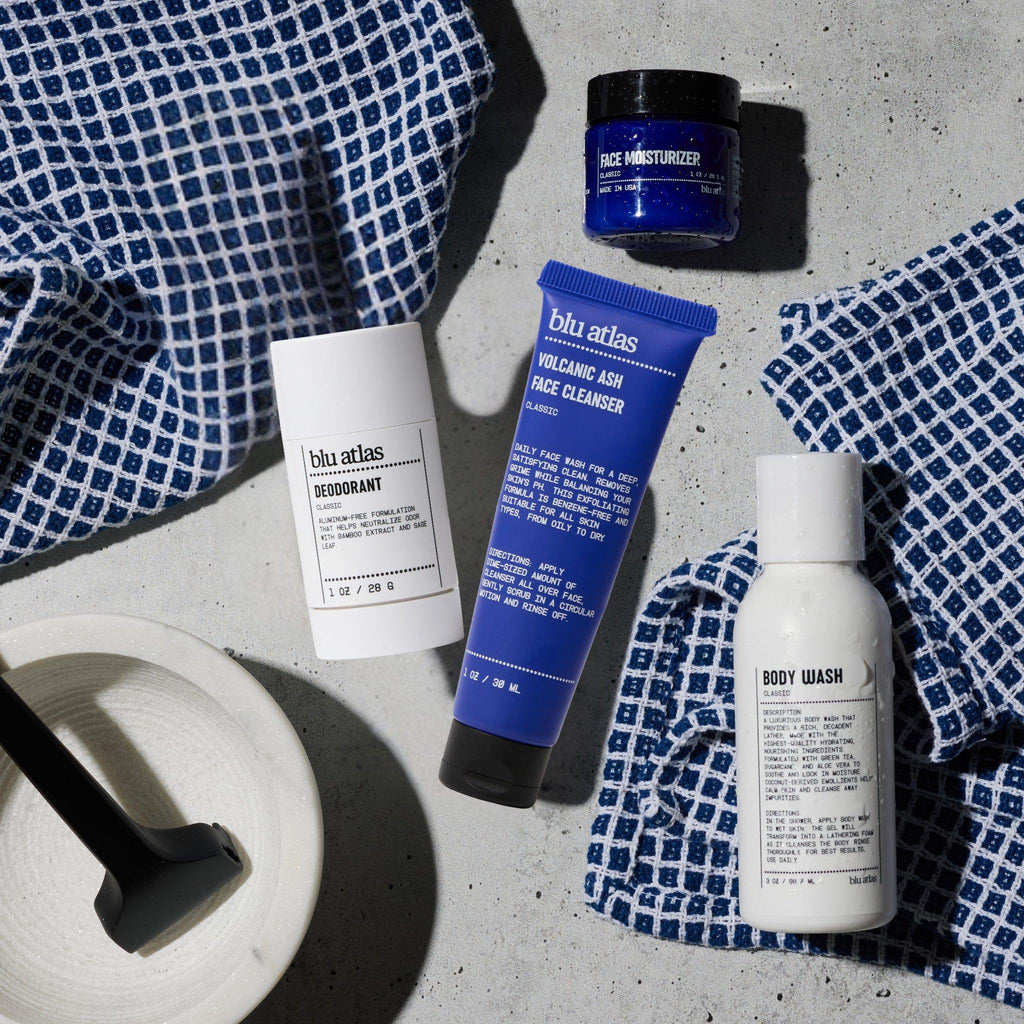 The Blu Atlas Bestseller Mini Bundle—including an aluminum-free men’s deodorant with Bamboo Extract, face cleanser, moisturizer, and body wash—is displayed on a textured surface with blue and white towels and a small brush.