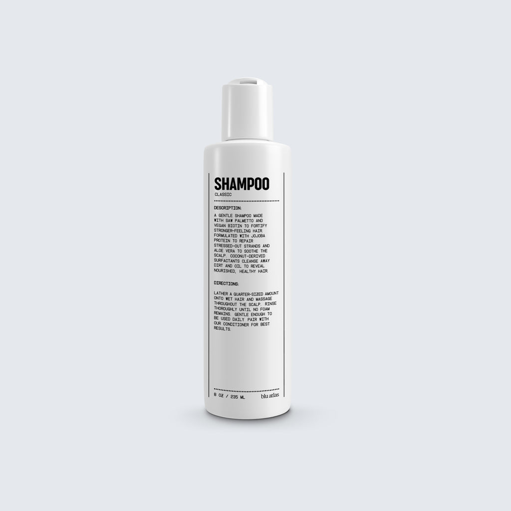 A shampoo bottle labeled with details in black text showcases ingredients such as jojoba protein and vegan biotin, along with usage instructions, comes from Blu Atlas's Natural Shampoo for All Hair Types line.