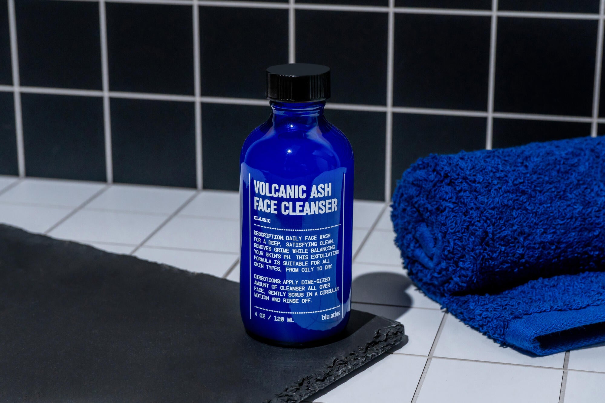 Blue bottle of volcanic ash face cleanser on a black towel with a blue towel in the background.