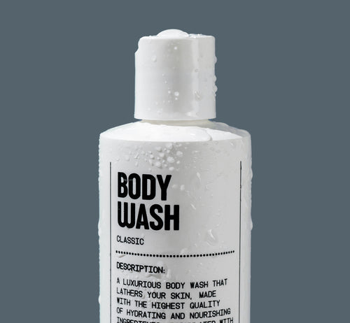 A white bottle labeled Natural Body Wash by Blu Atlas, with coconut-derived cleansers and water droplets on its surface, set against a plain gray background.