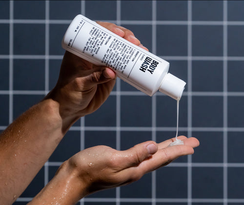 Someone pours Blu Atlas Natural Body Wash from a white bottle into their hand with tiled background visible.