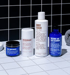 Experience the perfect Starter Set from Blu Atlas for your daily routine. Displayed on a tiled surface against a black-tiled wall, this set includes four personal care essentials: a face moisturizer, deodorant, body wash, and volcanic ash face cleanser to enhance your skin.