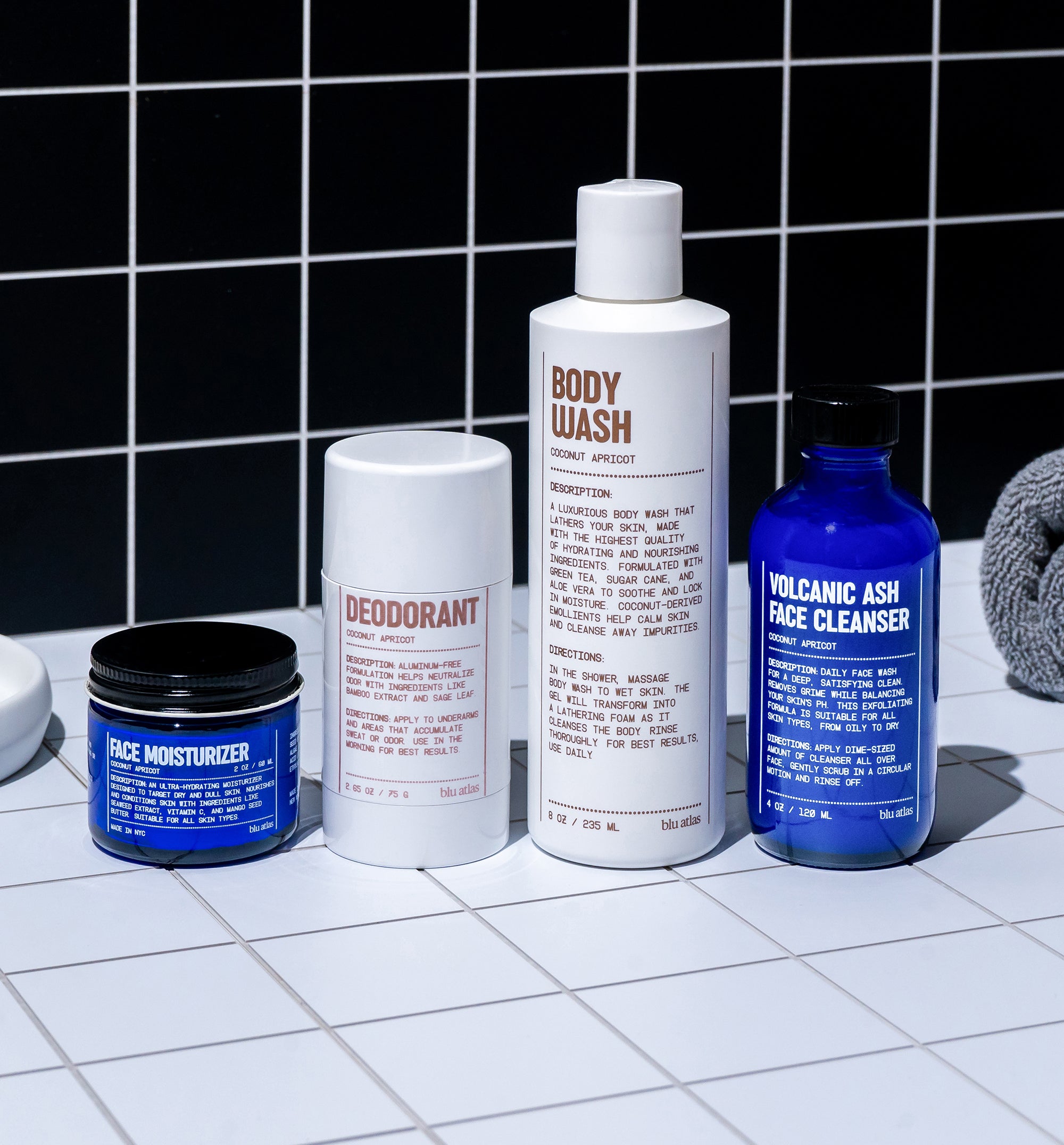 Experience the perfect Starter Set from Blu Atlas for your daily routine. Displayed on a tiled surface against a black-tiled wall, this set includes four personal care essentials: a face moisturizer, deodorant, body wash, and volcanic ash face cleanser to enhance your skin.