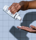 A person pours Blu Atlas Natural Conditioner into their palm from the bottle, with a tiled background in view.