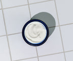 A container of Blu Atlas Hydrating Face Moisturizer for All Skin Types, enriched with seaweed extract, sits on a white tile surface with a grid pattern and features a blue rim.