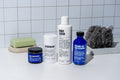 The Blu Atlas Starter Set, featuring deodorant, body wash, volcanic ash face cleanser, and face moisturizer, is elegantly displayed alongside a soap bar and loofah on a tiled surface. Ideal for elevating your daily routine and promoting healthier skin.