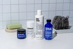 The Blu Atlas Starter Set, featuring deodorant, body wash, volcanic ash face cleanser, and face moisturizer, is elegantly displayed alongside a soap bar and loofah on a tiled surface. Ideal for elevating your daily routine and promoting healthier skin.