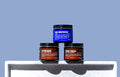 The Blu Atlas Shave Bundle, consisting of jars of face moisturizer, aftershave balm, and shave cream, is elegantly arranged on a white surface with a calming blue background.
