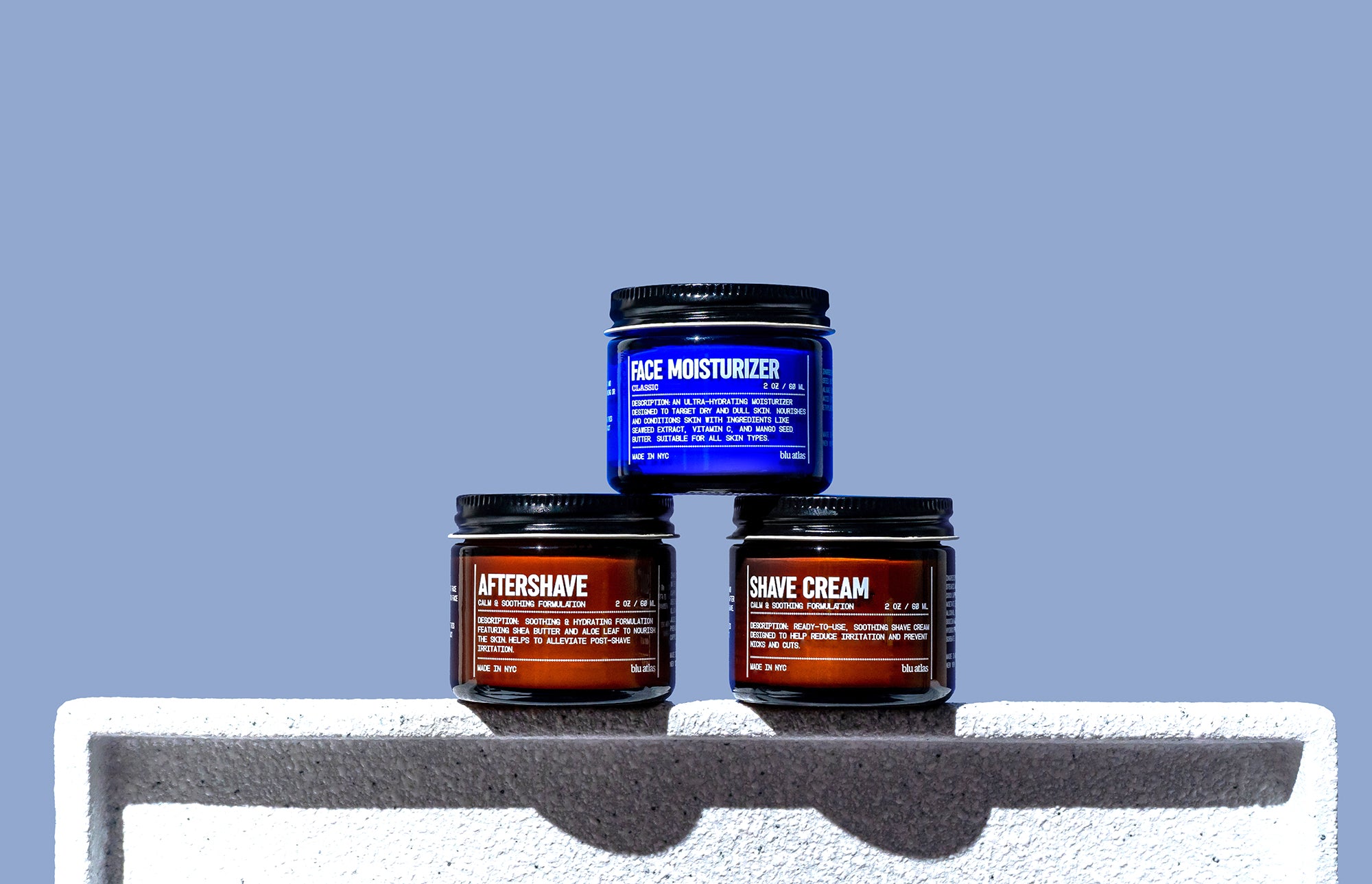 The Blu Atlas Shave Bundle, consisting of jars of face moisturizer, aftershave balm, and shave cream, is elegantly arranged on a white surface with a calming blue background.