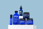 Introducing the Advanced Skincare Set by Blu Atlas, a remarkable collection of skincare products featuring soothing blue items such as the Volcanic Ash Face Cleanser, Vitamin C Serum, face mask, exfoliating scrub, moisturizer, and eye stick. These exquisite products are beautifully arranged on a white platform against a tranquil blue background.